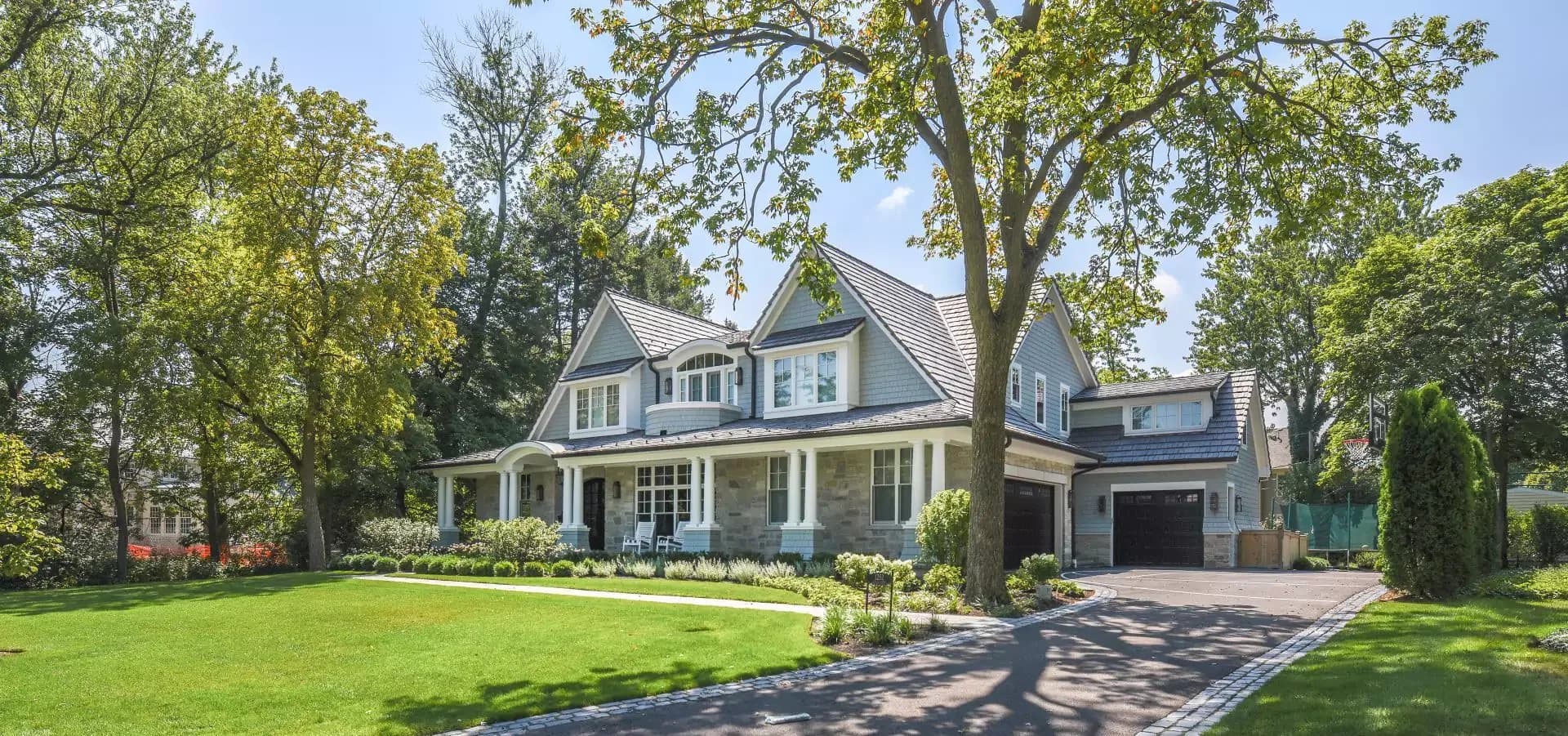 A blue shingled house with white trim, partial stone facade and an attached garage. A large green yard is out front.